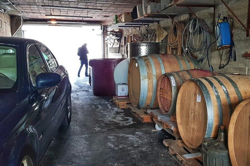 Een auto geparkeerd in een garage met houten vaten en slangen aan de muur. 3