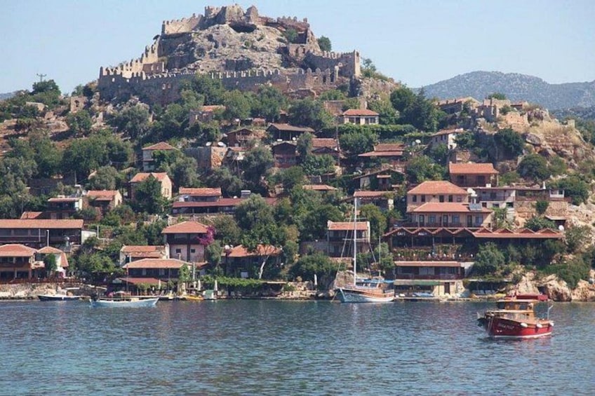 Un pueblo costero con un castillo histórico en una colina, barcos en el agua y casas con tejados rojos. 4