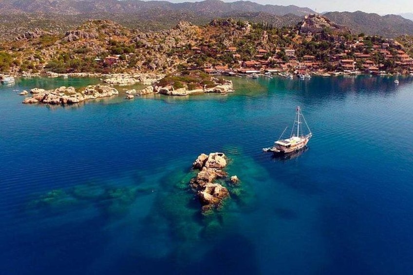 Un pueblo costero con aguas azul cristalino, un velero y afloramientos rocosos. 5