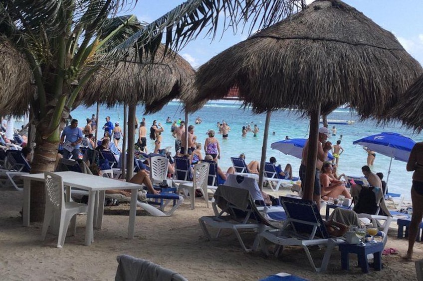 Een strand met rieten parasols, ligbedden en mensen die in het water zwemmen. 1