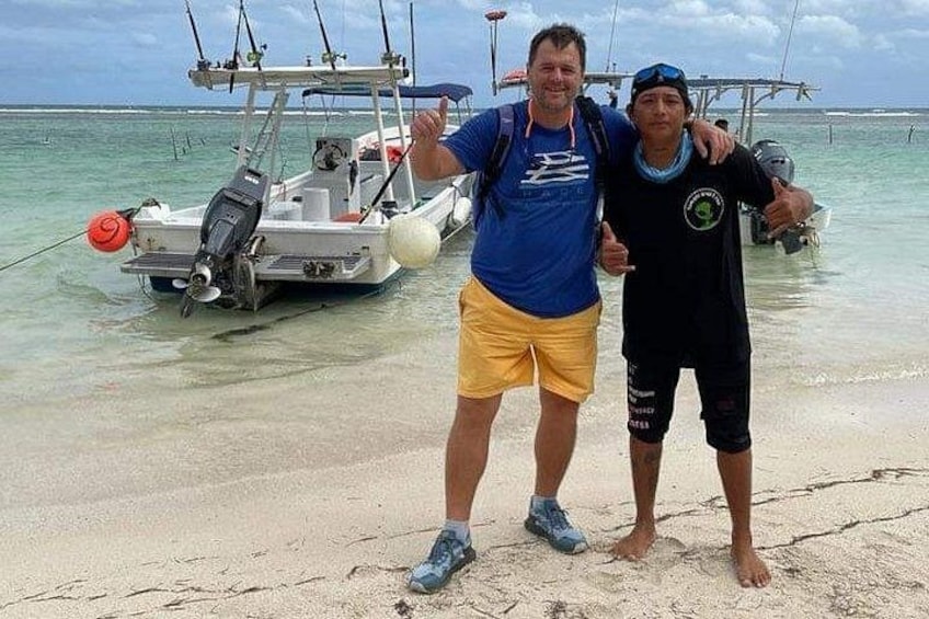 Twee personen staan op een zanderig strand, met een boot op de achtergrond. 5