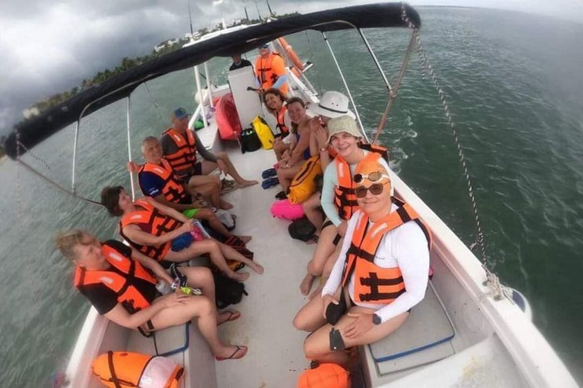 Een groep mensen in een boot, met reddingsvesten, met een rustige zee op de achtergrond. 4