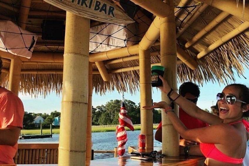 A tiki bar with a thatched roof, a person pouring a drink, and a red and white striped umbrella. 2