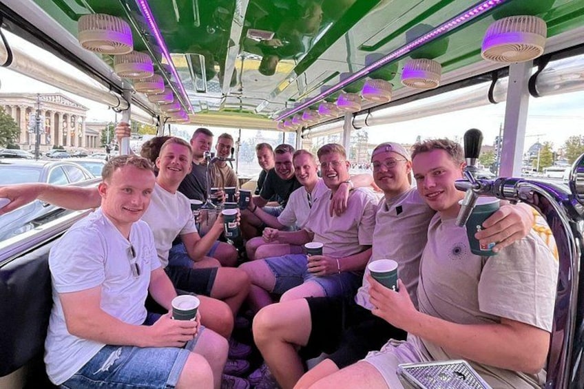 A group of people on a green bus with overhead lighting, holding coffee cups. 2
