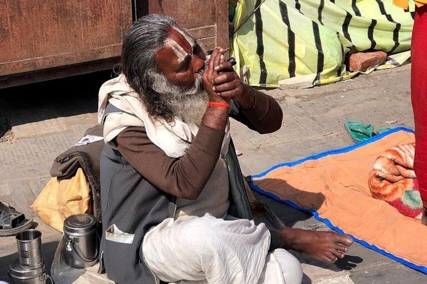 A person sitting on the ground with a blanket, a bag, and a thermos beside them. 2