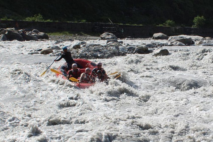Eine Gruppe von Menschen in einem roten Schlauchboot, das sich durch ein Flussstück mit Stromschnellen bewegt. 1