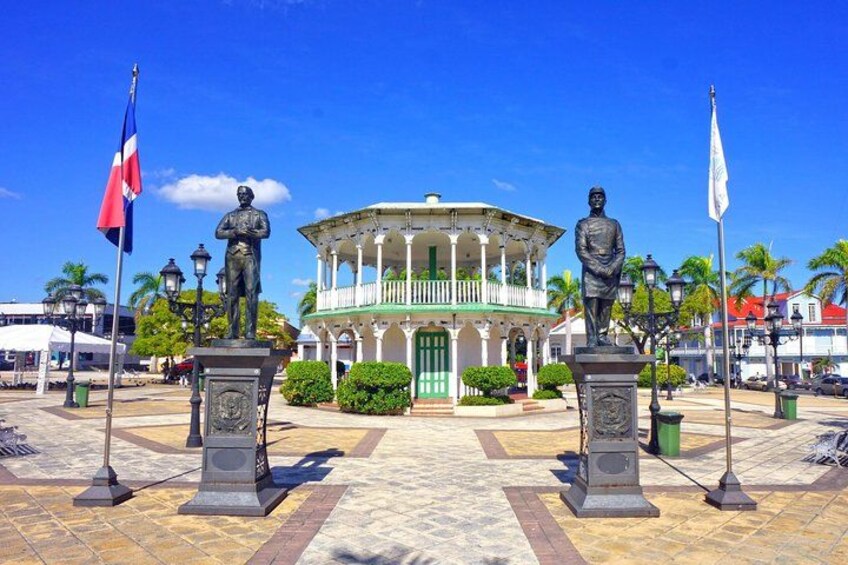 A colonial-style building with a central dome, flanked by two statues on pedestals, and flags on poles. 2
