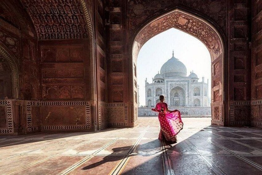 En person i en lyserød kjole går gennem en detaljeret arkade hen mod Taj Mahal. 3