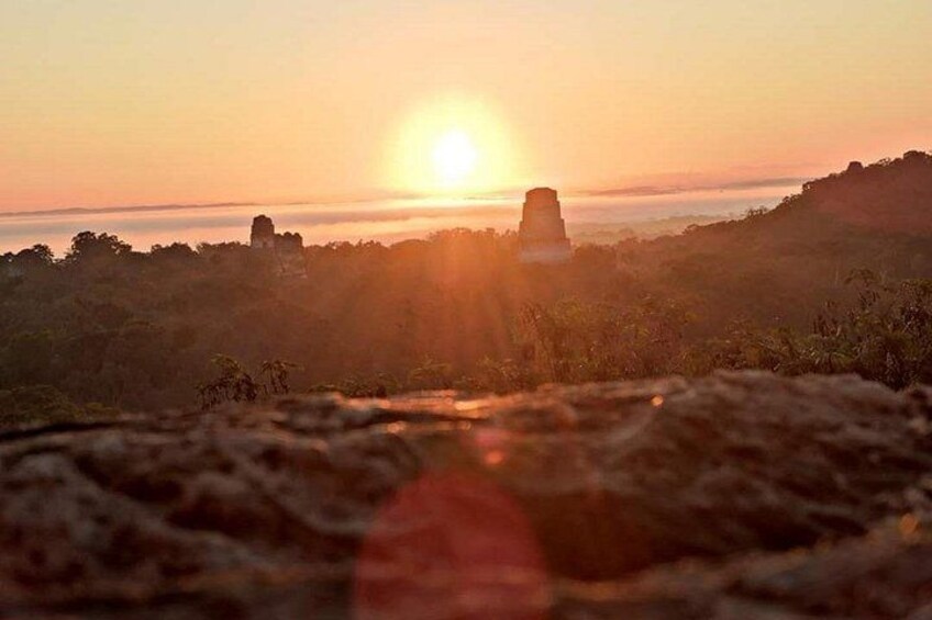 A sunset over a landscape with a prominent rock formation in the center. 1