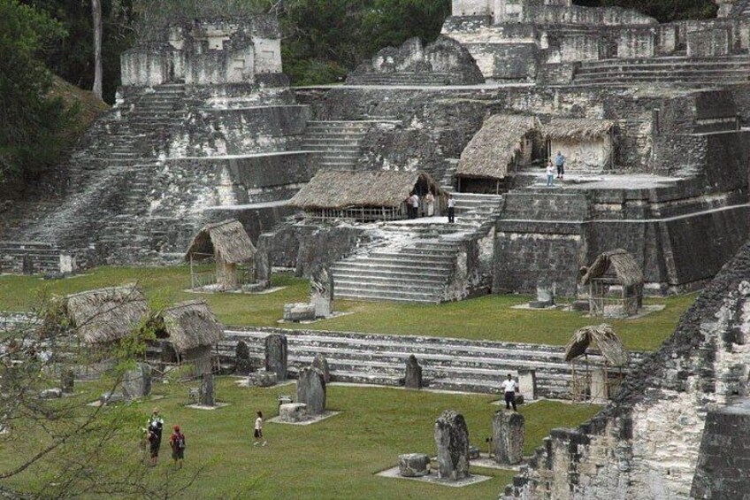 Ancient ruins with stepped platforms, stone structures, and thatched-roof huts. 3