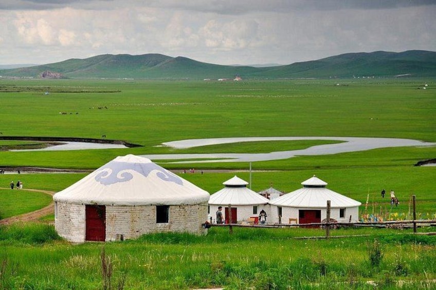 Three yurts in a grassy field with mountains in the background. 1
