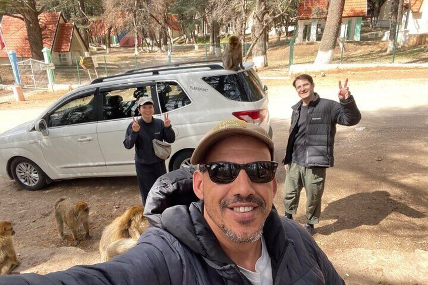 A person taking a selfie with a dog, a van, and two people in the background. 3