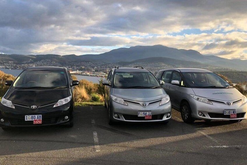 Drei Autos stehen an einer Straße, mit Blick auf Berge und eine Stadt im Hintergrund. 1