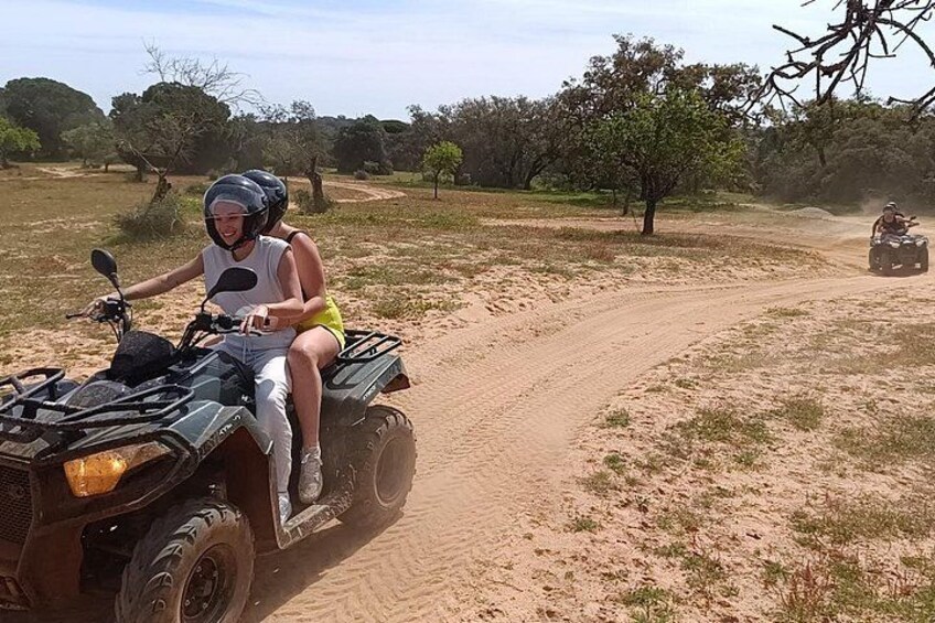 A person riding an ATV on a dirt path with sparse vegetation and trees in the background. 5