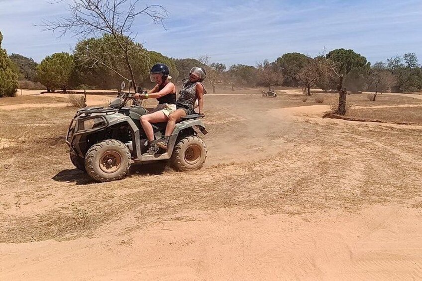 Two people on an ATV in a dry, open landscape with sparse trees and a clear sky. 4