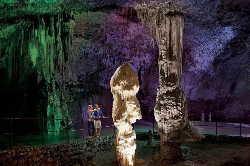 A cave with stalactites and a large stalagmite, illuminated by artificial lighting. 1