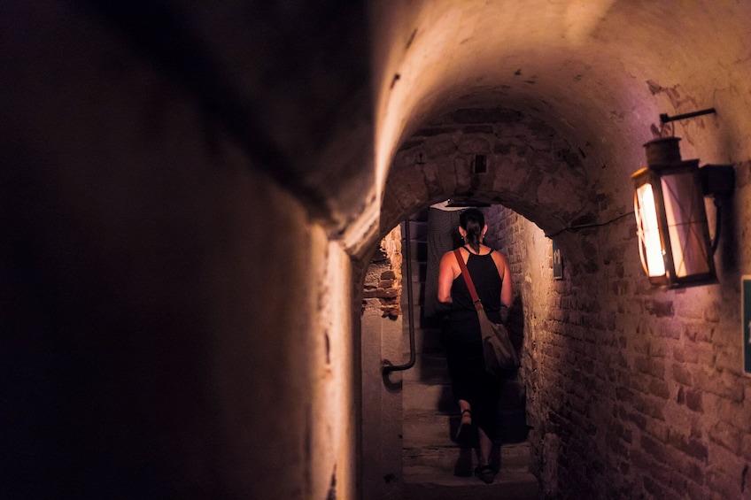 En person går gennem en svagt oplyst stengang med en lygte på væggen. 5