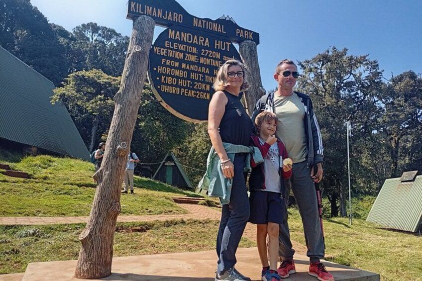 Una familia junto a un panel informativo sobre el Parque Nacional Kilimanjaro, que incluye la caba ña Mandara y la cima Uhuru. 1