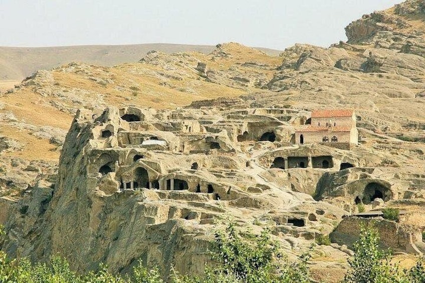 A rock-cut architecture with multiple cave-like structures and a small building with a red roof. 3