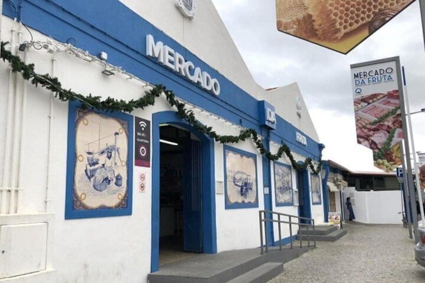Ein Gebäude mit einer blau-weißen Fassade, geschmückt mit festlichen Girlanden, und einem Schild mit der Aufschrift 'MERCADO DA FRUTA'. 2