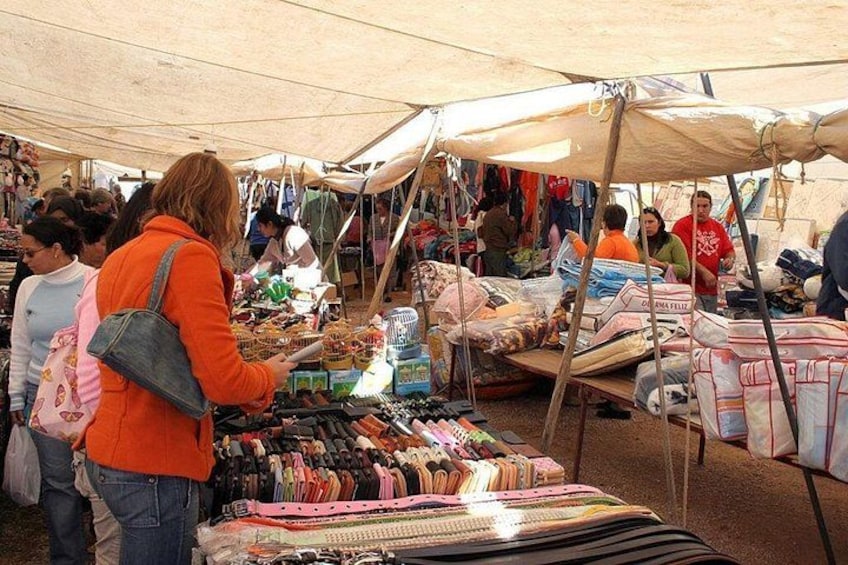 Un mercado con gente comprando bajo carpas, diversos productos expuestos y un ambiente concurrido. 1