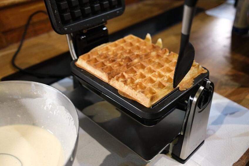 A waffle iron with a waffle inside, a bowl of batter, and a spatula. 5