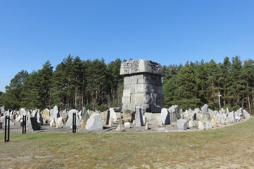 A stone monument surrounded by large rocks, with a forest in the background. 5