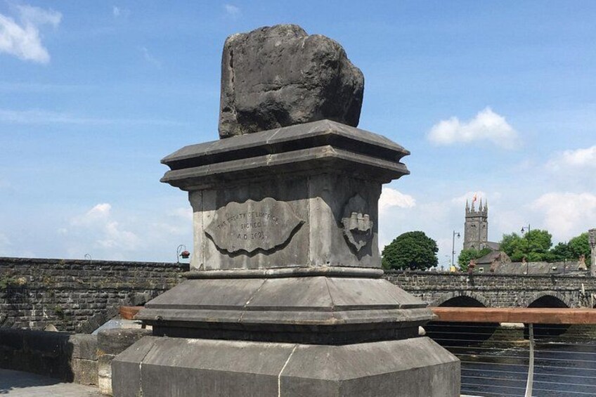 A stone monument with inscriptions, a stone wall, and a tower in the background. 3