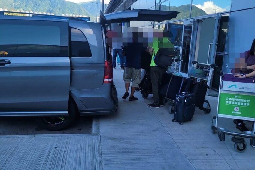 A vehicle parked at a terminal with people and luggage nearby. 4