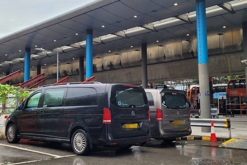A parking area with two vans, a bus, and a building with blue pillars. 5