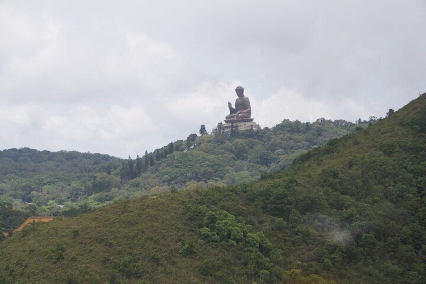 A large seated statue on a hilltop, surrounded by dense forest. 3