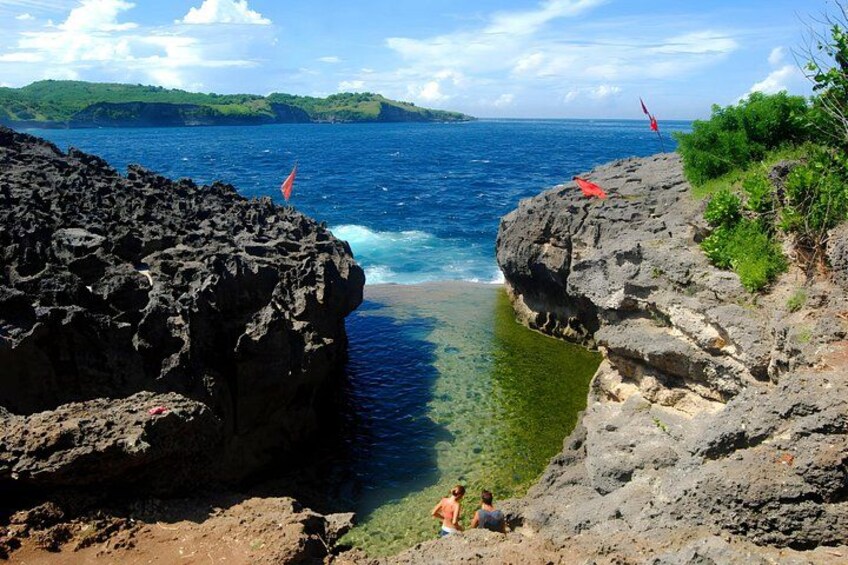 A coastal landscape with rocky cliffs, clear blue water, and a flag on a cliff. 3