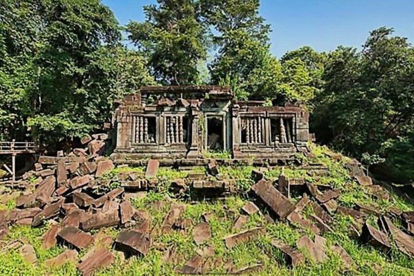 An ancient temple structure surrounded by overgrown vegetation and scattered stone debris. 4