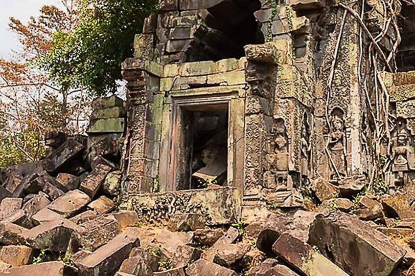 A ruined temple with a central doorway, overgrown vegetation, and scattered stones. 2