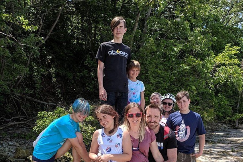 A group of people outdoors, some wearing casual clothing, with trees and greenery in the background. 2