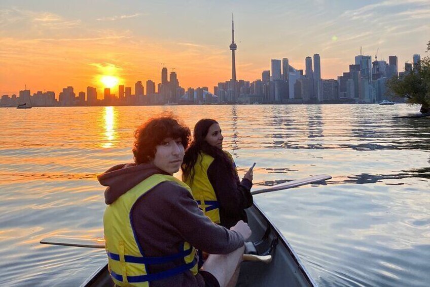 Two people in a canoe on a river with a city skyline in the background during sunset. 2