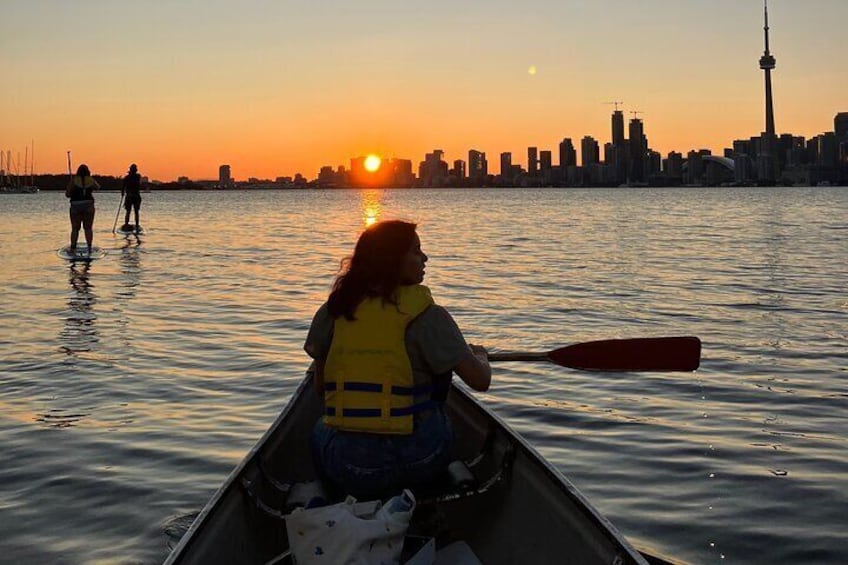 A person in a canoe paddling during sunset with a city skyline in the background. 4