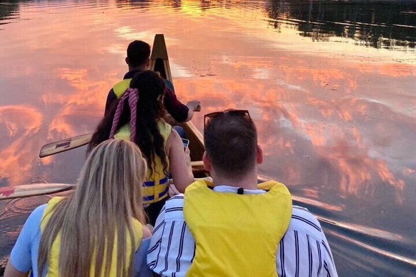 Three people in a canoe on a calm body of water during sunset. 1