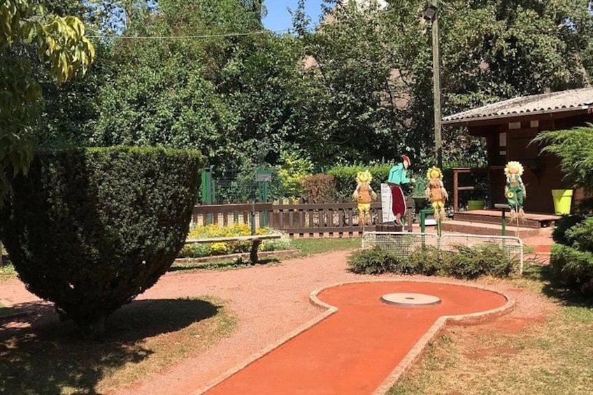 A garden with a large topiary, a red pathway, and a small building. 2