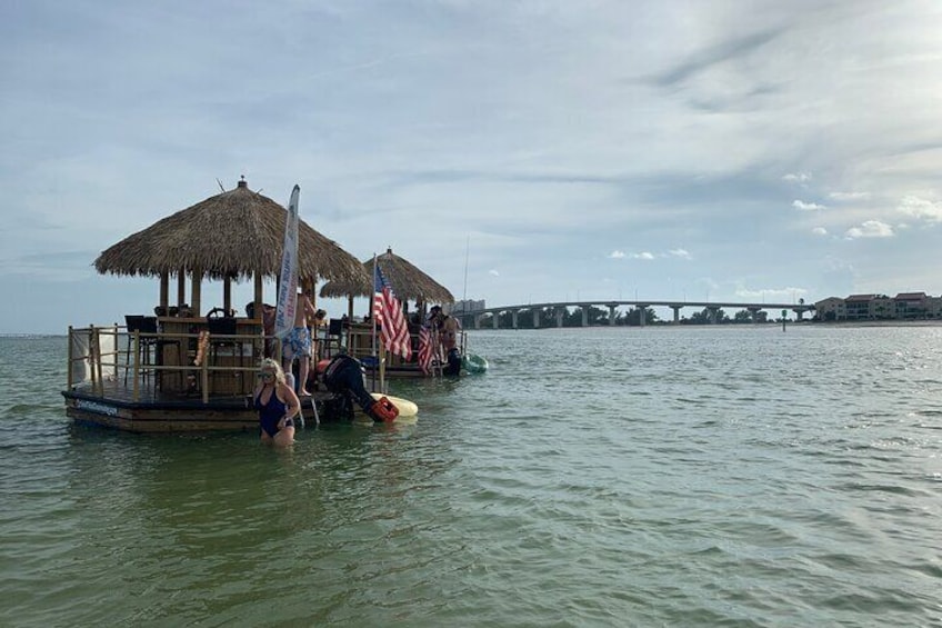 Un bateau doté d’un toit de chaume et arborant des drapeaux américains, amarré dans des eaux calmes, avec un pont en arrière-plan. 1