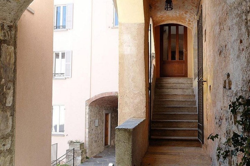 A narrow stone staircase leading to a wooden door, flanked by buildings with balconies and windows. 2