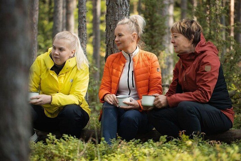 Trois personnes sont assises sur le sol de la forêt, chacune tenant une tasse. 2