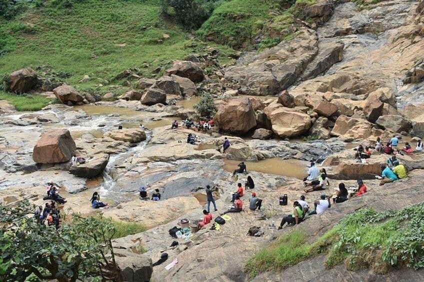 Un letto di fiume roccioso con persone sedute e in piedi, circondato da grandi massi e vegetazione. 5