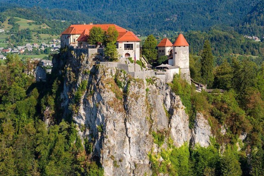 A castle on a cliff with a red roof, surrounded by greenery and mountains. 3