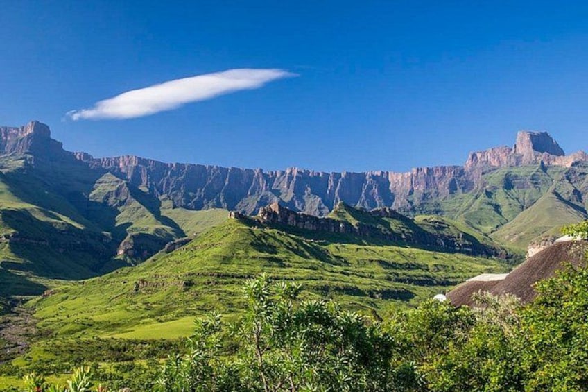 Un paysage montagneux avec des collines verdoyantes et des falaises rocheuses, le tout sous un ciel bleu dégagé. 1