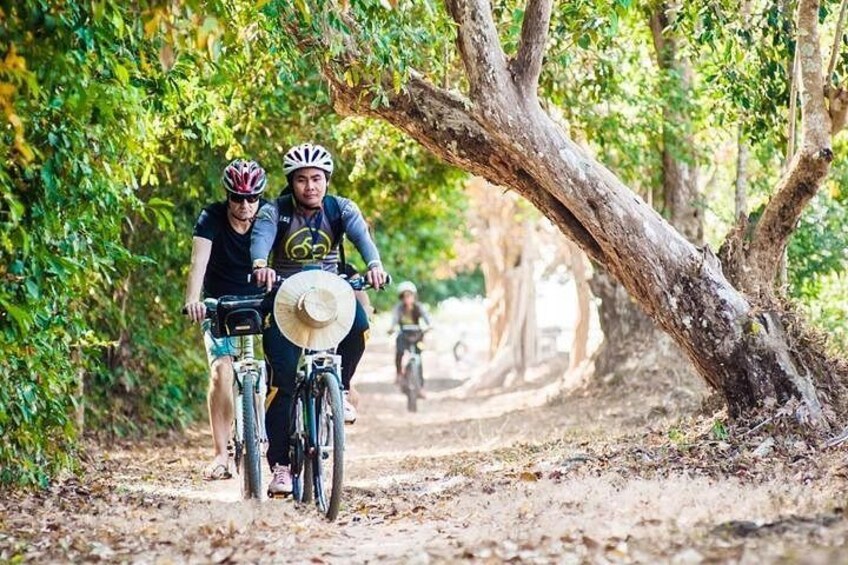 Two cyclists on a dirt path surrounded by trees. 1