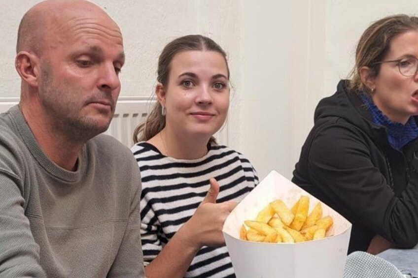 Three people sitting at a table with a box of fries. 3