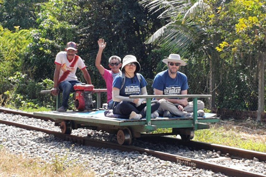 Four people on a train cart on a railway track surrounded by greenery. 1