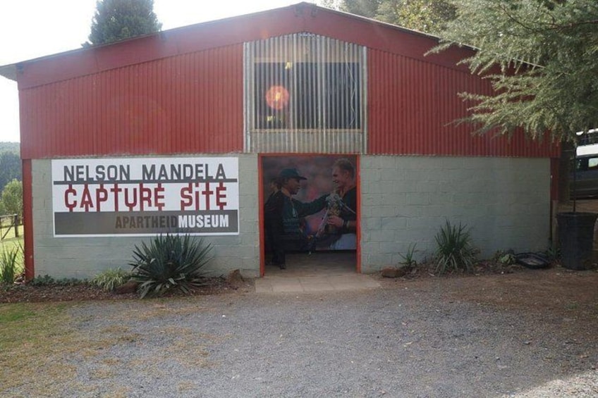 A red building with a sign reading 'Nelson Mandela Capture Site Apartheid Museum.' 2
