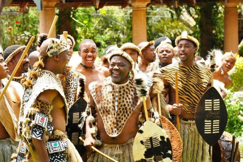 A group of people in traditional attire, holding spears and shields, in a natural outdoor setting. 4
